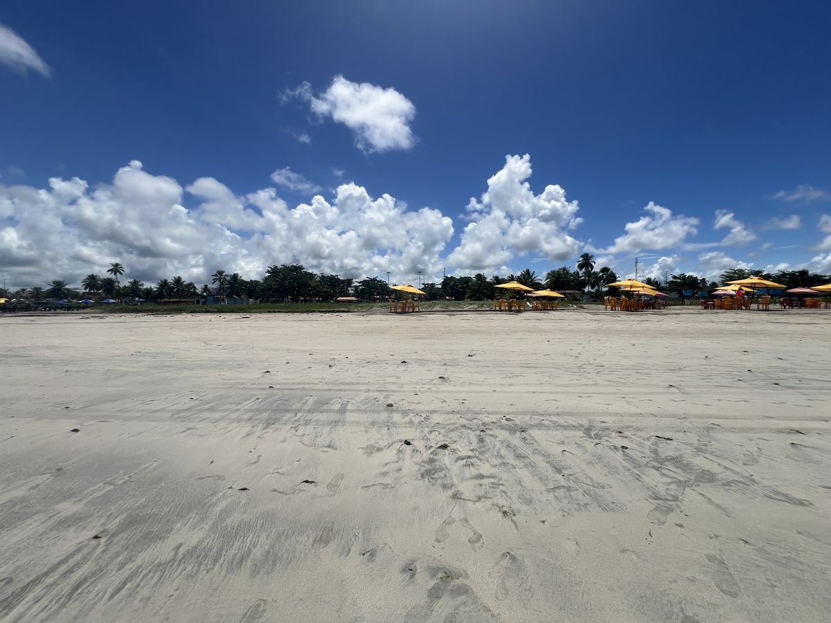 Turistas relaxando em cadeiras de praia sob guarda-sóis na orla de Paripueira com mar azul ao fundo